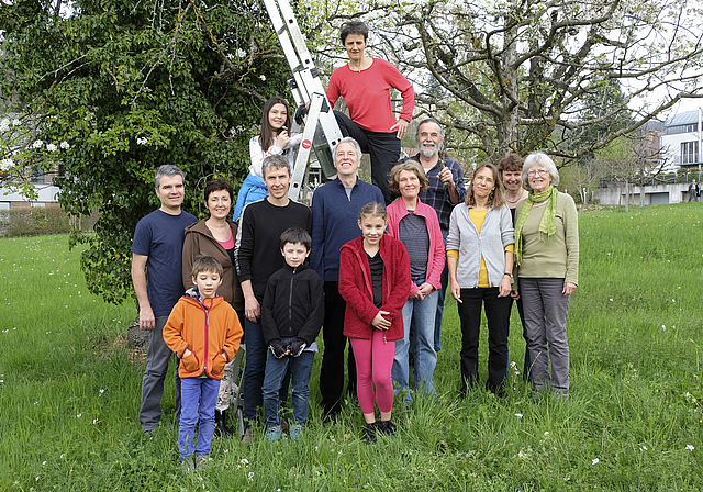 Familiäre Atmosphäre: Mitglieder der Trägerschaft Obstbaumgarten Badhof vor einem mit Efeu bewachsenen Baum.
