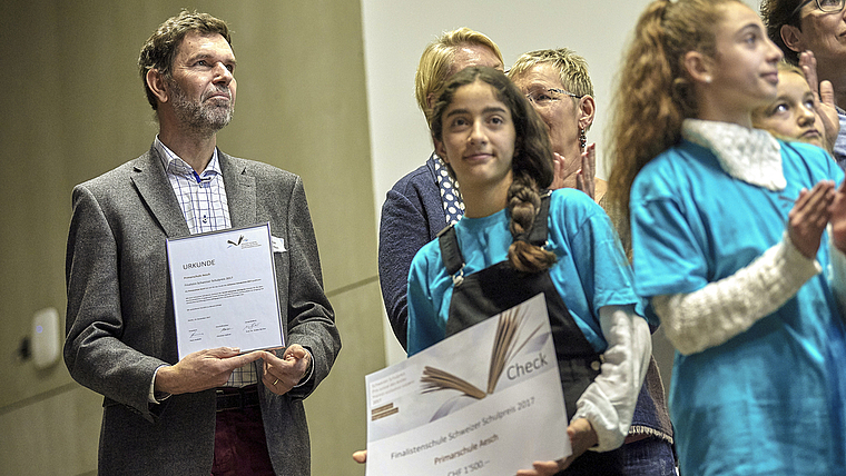 Eine Urkunde und 1500 Franken: Niggi Thurnherr, Schulleiter der Primarstufe Aesch, und eine Schülerin mit den verdienten «Trophäen» anlässlich der Verleihung des Schweizer Schulpreises am 13. Dezember in Bern.  Foto: ZVG/Adrian Moser