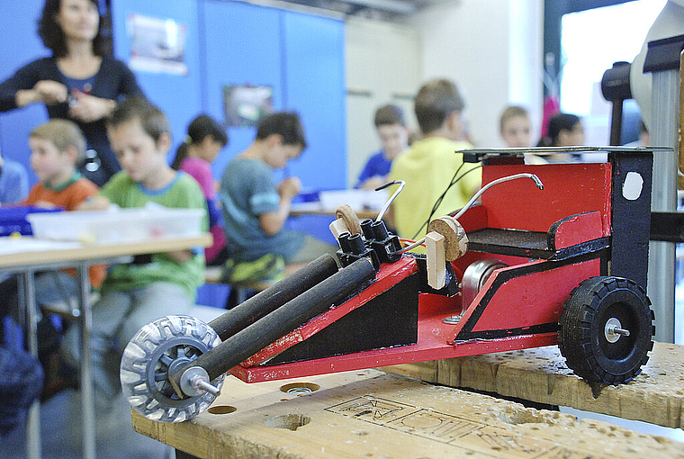 Ferienpass-Werkstatt: Im Vordergrund ein fertiger Prototyp eines Solar-Trikes, im Hintergrund eifrig arbeitende Kinder. Foto: Brunnschweiler