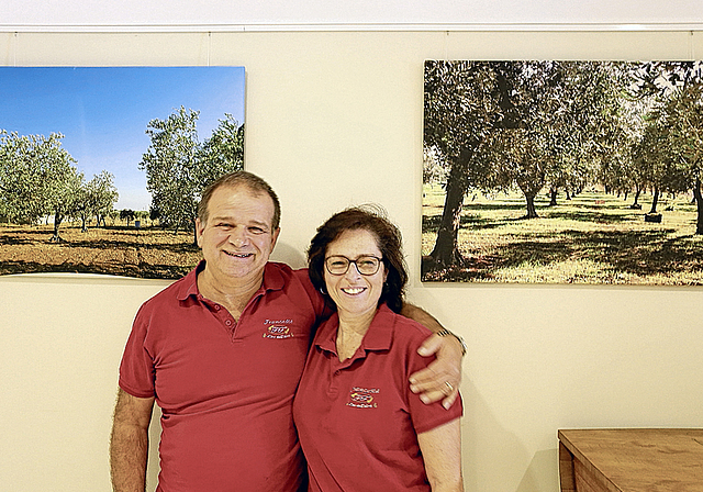 Besitzen benachbarte Olivenplantagen: Francesco Augello und Francesca Augello jeweils vor dem Bild ihrer eigenen Olivenplantage. Foto: Simone Pürro